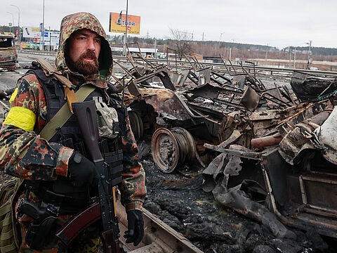 Ein Kämpfer eines ukrainischen Freiwilligenverbandes steht bei der Stadt Bucha vor ausgebrannten russischen Militärfahrzeugen. Foto: picture alliance / Associated Press / Serhii Nuzhnenko