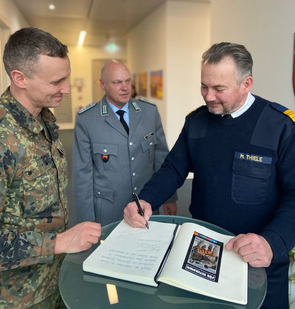 Oberstleutnant i.G. Marcel Bohnert (l.) und Fregattenkapitän Marco Thiele tragen sich ins Gästebuch des Veteranenbüros ein. Im Hintergrund: Der Leiter des Büros, Oberstleutnant Michael Krause. Foto: DBwV/Jasmina Perske