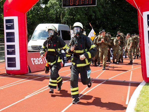 Voller Einsatz: Trotz der Wärme laufen diese beide Feuerwehrmänner in voller Montur und unter Atemschutz mit. Dahinter schließen sich Soldaten mit großen Rucksäcken an. Foto: DBwV/Vieth