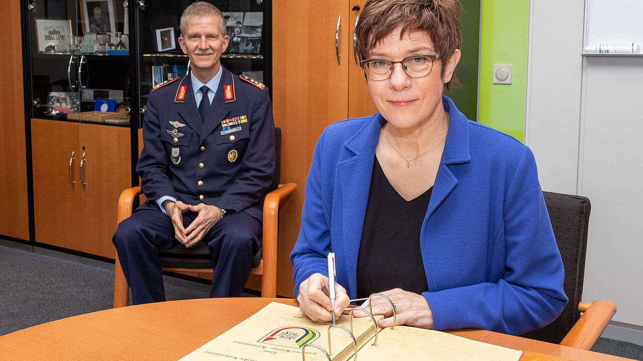 Verteidigungsministerin Annegret Kramp-Karrenbauer trägt sich unter den Augen von Generalleutnant Martin Schelleis in das Gästebuch des Kommando SKB (Streitkräftebasis) ein. Foto: Twitter/Streitkräftebasis