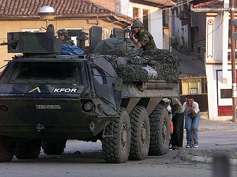 Einsatz im Kosovo: Zivilisten suchen am 13. Juni 1999 in Prizren Deckung hinter einem Transportpanzer der Bundeswehr. Bei dem Schusswechsel kommen zwei bewaffnete serbische Angreifer ums Leben. Foto: picture-alliance/dpa/AFP Christophe Simon
