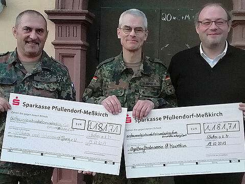 Oberst Jochen Gumprich (Mitte) übergibt die Spendenschecks in Höhe von jeweils 1.181,71 Euro an Pfarrer Markus Manter (r.) für den Orgelbauförderverein. Für die Soldaten und Veteranen Stiftung nahm Oberstleutnant Josef Rauch, der stellvertretende Vorsitzende des Landesverbandes Süddeutschland, den Scheck entgegen. Foto: SVS