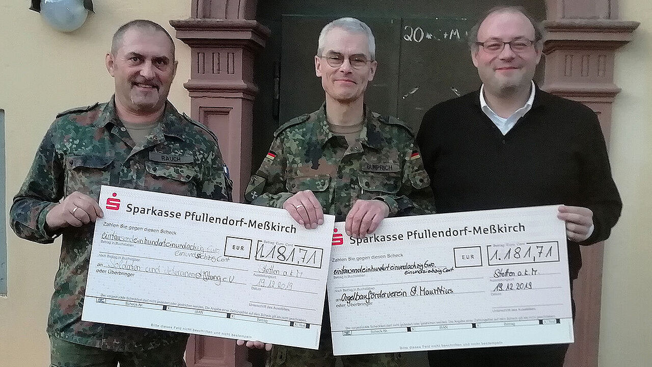 Oberst Jochen Gumprich (Mitte) übergibt die Spendenschecks in Höhe von jeweils 1.181,71 Euro an Pfarrer Markus Manter (r.) für den Orgelbauförderverein. Für die Soldaten und Veteranen Stiftung nahm Oberstleutnant Josef Rauch, der stellvertretende Vorsitzende des Landesverbandes Süddeutschland, den Scheck entgegen. Foto: SVS