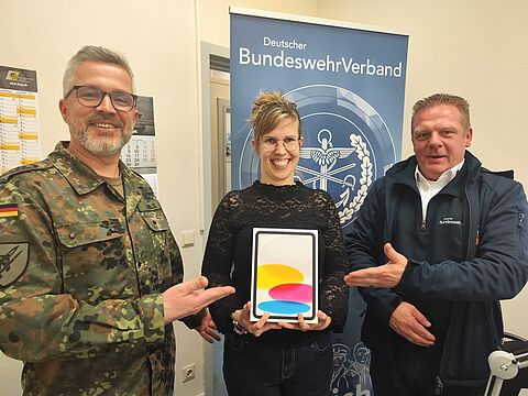 Stabsfeldwebel Sven Wille, Vorsitzender der Truppenkameradschaft Luftwaffe, und Außendienstmitarbeiter Björn Hellmund übereichen Gewinnerin Anne Scholz ein neues iPad. Foto: DBwV