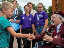 Kinder und Jugendliche bedanken sich beim 97-jährigen John Jeffries anlässlich der Einweihung einer Skulptur im Jahr 2019. Der Weltkriegsveteran und ehemalige Fallschirmspringer verstarb im Folgejahr. Foto: Ministry of Defense