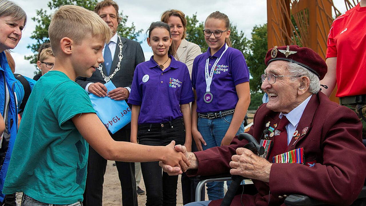Kinder und Jugendliche bedanken sich beim 97-jährigen John Jeffries anlässlich der Einweihung einer Skulptur im Jahr 2019. Der Weltkriegsveteran und ehemalige Fallschirmspringer verstarb im Folgejahr. Foto: Ministry of Defense