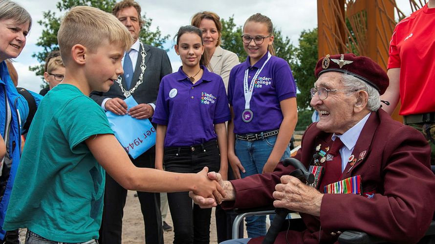 Kinder und Jugendliche bedanken sich beim 97-jährigen John Jeffries anlässlich der Einweihung einer Skulptur im Jahr 2019. Der Weltkriegsveteran und ehemalige Fallschirmspringer verstarb im Folgejahr. Foto: Ministry of Defense