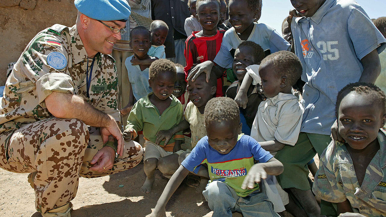 Symbolbild: Ein Oberstleutnant unterhält sich im April 2006 mit Flüchtlingskindern im Binnenflüchtlingslager Jebel Aulia. Foto: Bundeswehr/Rott 