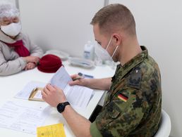 Ein Fliegerarzt führt mit einer zu impfenden Person ein Vorgespräch im Corona-Impfzentrum am Flughafen BER in Schönefeld im Rahmen der Amtshilfe während der Corona-Pandemie. Die Soldatinnen und Soldaten sind in der Amtshilfe einem erhöhten Infektionsrisiko ausgesetzt und müssen entsprechend geschützt werden. Foto: Bundeswehr/Tom Twardy