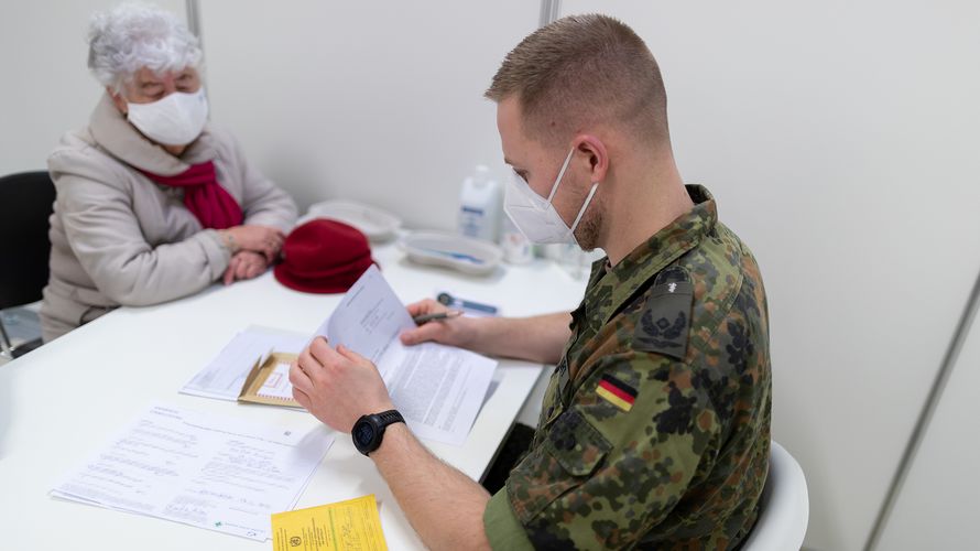 Ein Fliegerarzt führt mit einer zu impfenden Person ein Vorgespräch im Corona-Impfzentrum am Flughafen BER in Schönefeld im Rahmen der Amtshilfe während der Corona-Pandemie. Die Soldatinnen und Soldaten sind in der Amtshilfe einem erhöhten Infektionsrisiko ausgesetzt und müssen entsprechend geschützt werden. Foto: Bundeswehr/Tom Twardy