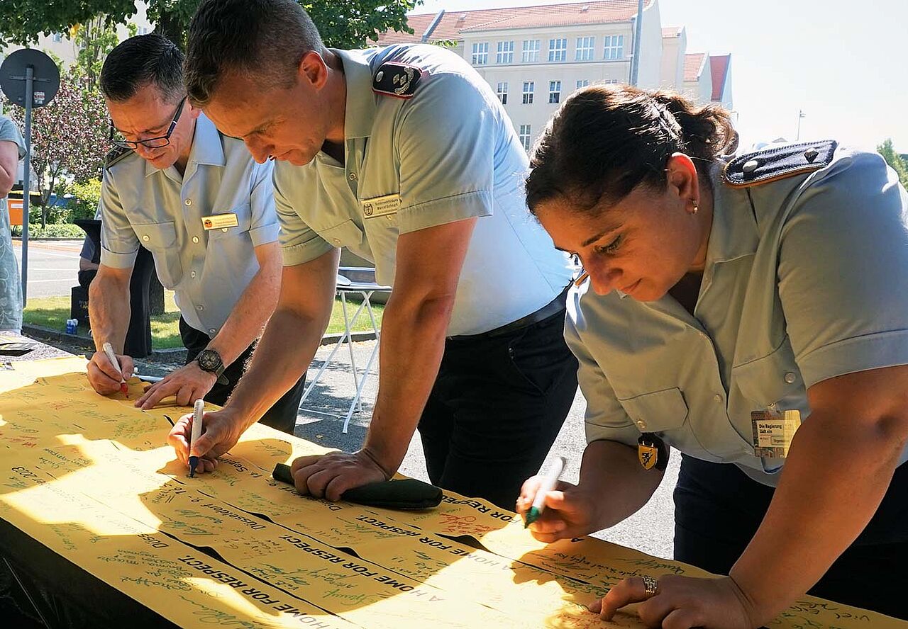 Die stellvertretenden Bundesvorsitzenden Stabsfeldwebel Thomas Schwappacher und Oberstleutnant i.G. Marcel Bohnert sowie die stellvertretende Vorsitzende Luftwaffe, Leutnant Hülya Süzen, unterschreiben am Invictus-Games-Truck ein Gelbes Band der Solidarität.