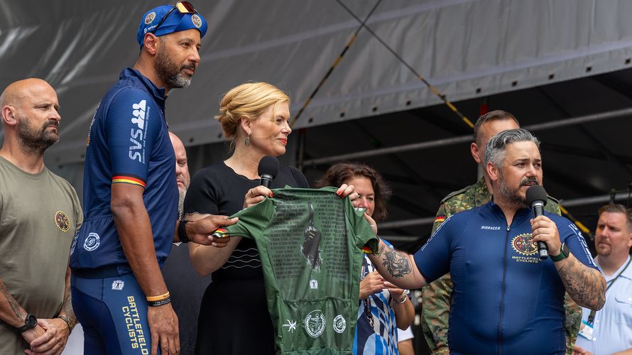 Auf dem Rad fuhren sie über 600 Kilometer nach Berlin: Die Biker der "Tour of Valor". Am Veteranentag übergaben Stefan Huss (rechts, mit Mikro) und Naef Adebahr (2.v.l.) ein Sondertrikot an die Schirmfrau des Veteranentages, Julia Klöckner. Foto: DBwV/Yann Bombeke