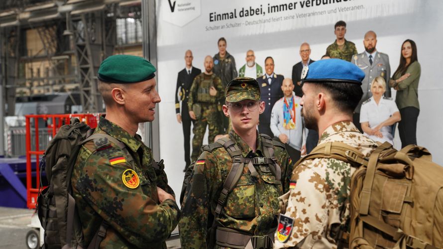 Oberstleutnant i.G. Marcel Bohnert (links) im Gespräch mit zwei reisenden Soldaten am Hauptbahnhof in Frankfurt am Main – im Hintergrund ein Plakat der Bundesregierung zum Nationalen Veteranentag am 15. Juni 2025. Foto: Lars Brinkmann/LCB Photography