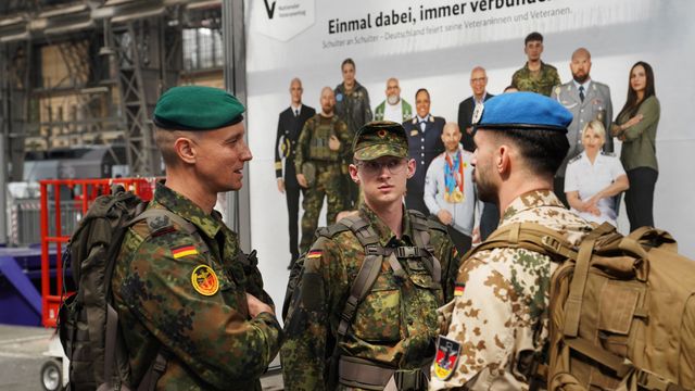Oberstleutnant i.G. Marcel Bohnert (links) im Gespräch mit zwei reisenden Soldaten am Hauptbahnhof in Frankfurt am Main – im Hintergrund ein Plakat der Bundesregierung zum Nationalen Veteranentag am 15. Juni 2025. Foto: Lars Brinkmann/LCB Photography
