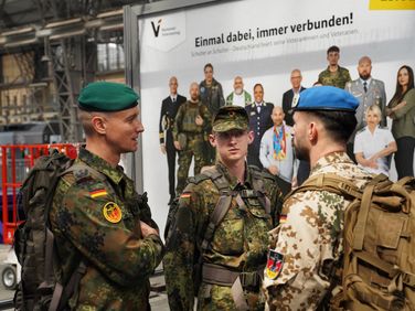 Oberstleutnant i.G. Marcel Bohnert (links) im Gespräch mit zwei reisenden Soldaten am Hauptbahnhof in Frankfurt am Main – im Hintergrund ein Plakat der Bundesregierung zum Nationalen Veteranentag am 15. Juni 2025. Foto: Lars Brinkmann/LCB Photography