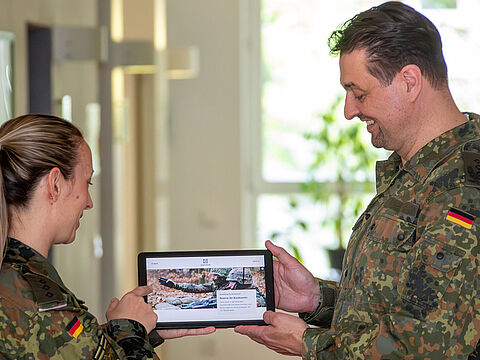 Eine Soldatin und ein Soldat haben ein Tablet in der Hand und schauen auf die Startseite der Internetseite der Reserve der Bundeswehr.