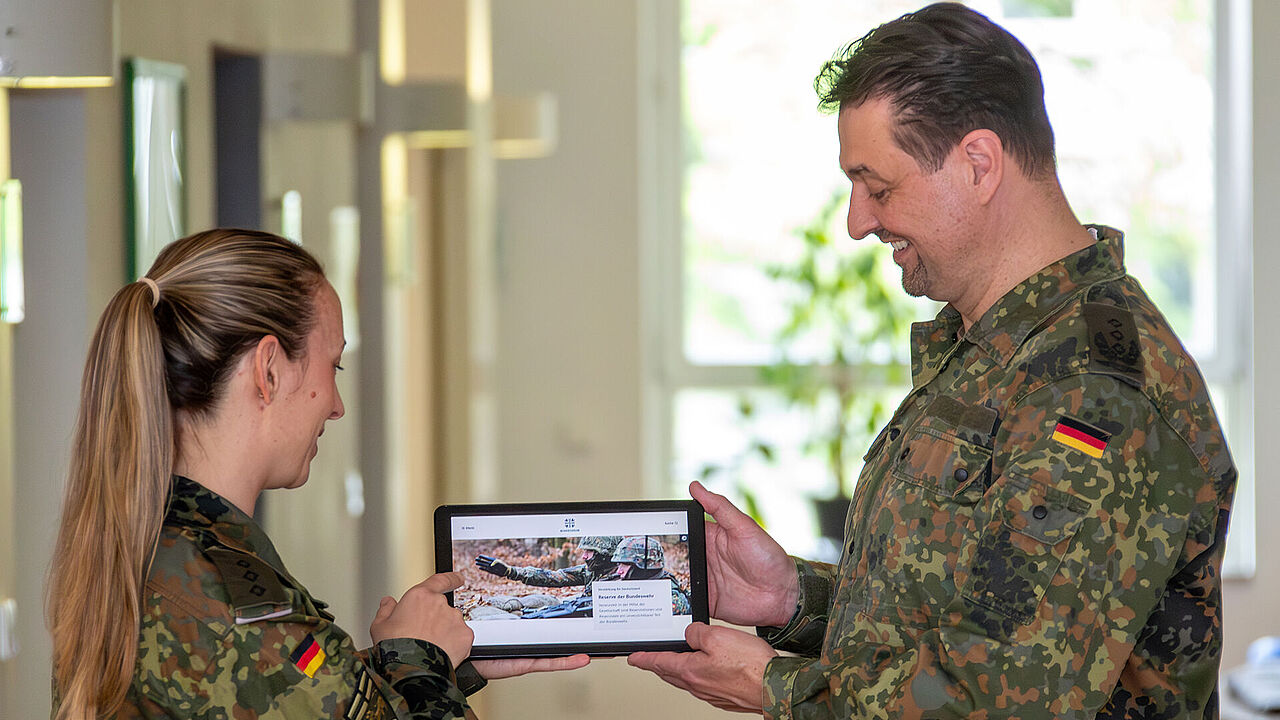 Eine Soldatin und ein Soldat haben ein Tablet in der Hand und schauen auf die Startseite der Internetseite der Reserve der Bundeswehr.