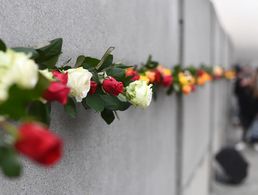Teilnehmer einer Gedenkveranstaltung zum 29. Jahrestag des Mauerfalls stecken am Mauerdenkmal Bernauer Straße Rosen zwischen Reste der ehemaligen Berliner Mauer. Foto: Ralf Hirschberger/dpa