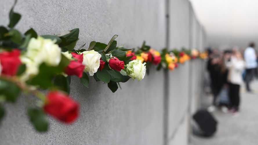 Teilnehmer einer Gedenkveranstaltung zum 29. Jahrestag des Mauerfalls stecken am Mauerdenkmal Bernauer Straße Rosen zwischen Reste der ehemaligen Berliner Mauer. Foto: Ralf Hirschberger/dpa