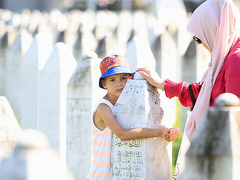 Gedenken zum 29. Jahrestag des Massakers von Srebrenica: Ein bosnischer Junge mit seiner Mutter an einem Grabstein in der Gedenkstätte in Potocari unweit von Srebrenica. Foto: picture alliance/REUTERS/Amel Emric